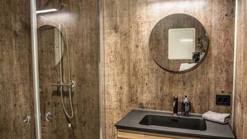 Un bagno moderno con doccia in vetro, mobile lavabo in legno e specchio tondo.