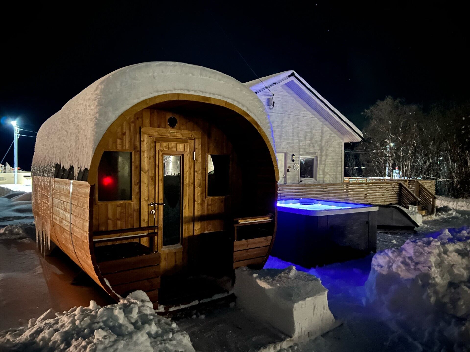Eine Holzhütte mit Tür und Fenstern, ein Pool mit blauer Beleuchtung sowie ein Gebäude im Hintergrund.