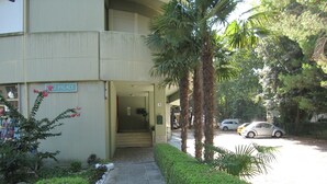 Entrada de um edifício com uma placa indicando 'Palace', um caminho pavimentado e carros estacionados.