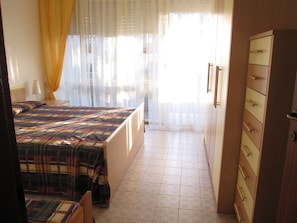 A bedroom with a bed, a chair, a wardrobe, and a window with curtains.