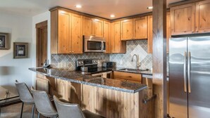 Eine moderne Küche mit Holzschränken, Granit Arbeitsplatten, Edelstahlgeräten und einer Bar mit Sitzgelegenheiten.