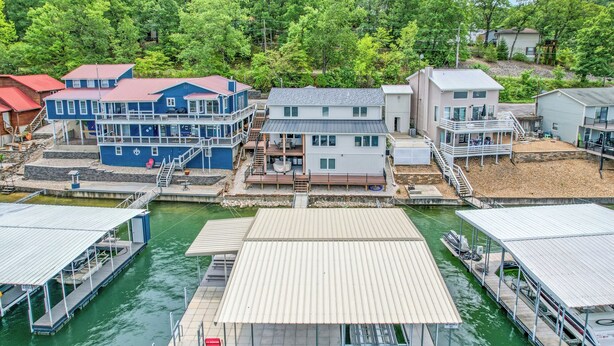 Une propriété située au bord de l’eau, comprenant plusieurs bâtiments, des quais et un espace central ouvert avec une terrasse couverte.