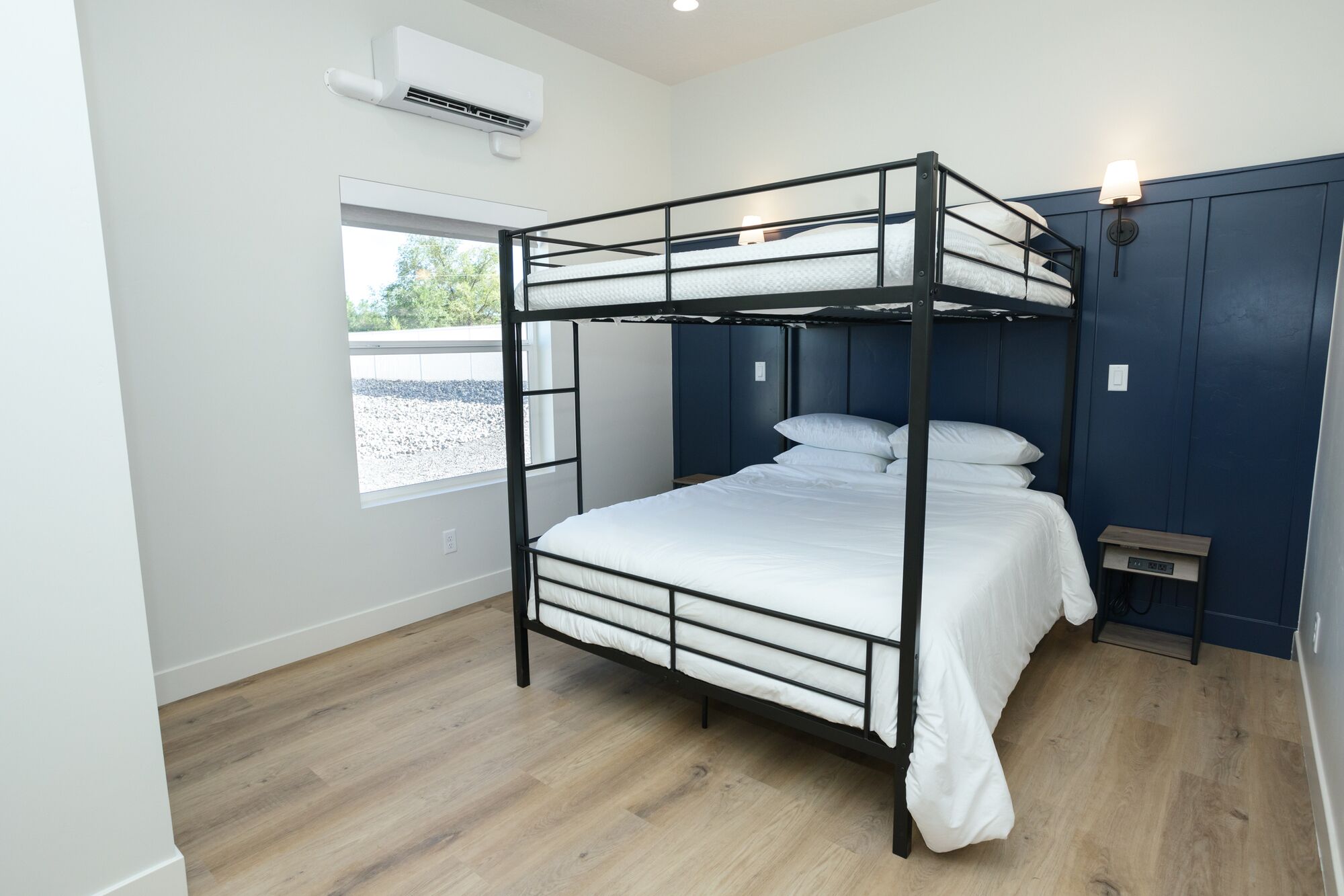 Habitación con literas, ventana, aire acondicionado de pared y mesita de noche con lámpara.