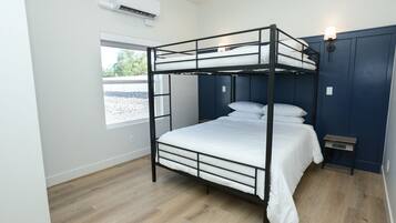 Habitación con literas, ventana, aire acondicionado de pared y mesita de noche con lámpara.