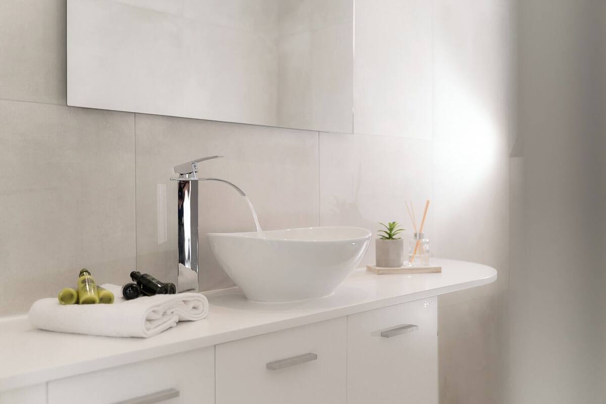 A modern bathroom with a white sink, chrome faucet, and a bowl sink. There is a towel and a small plant on the counter.
