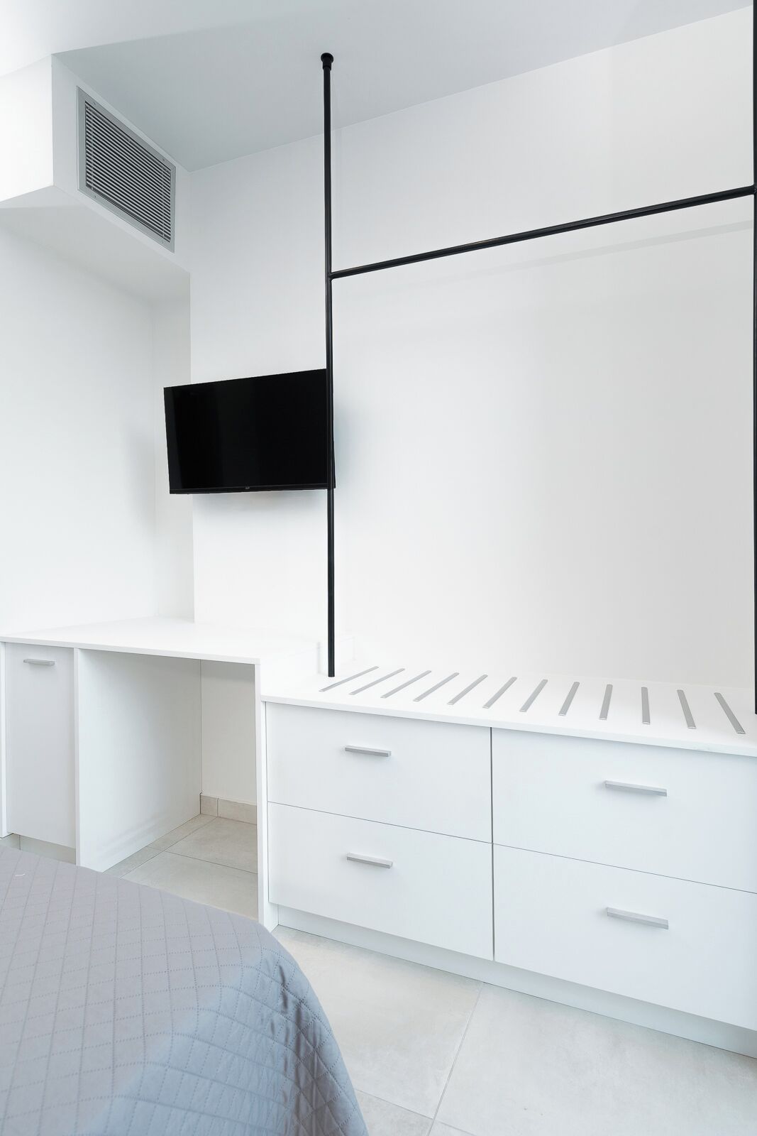 A modern bedroom with a bed, a white wardrobe, a TV mounted on the wall, and a ventilation system.