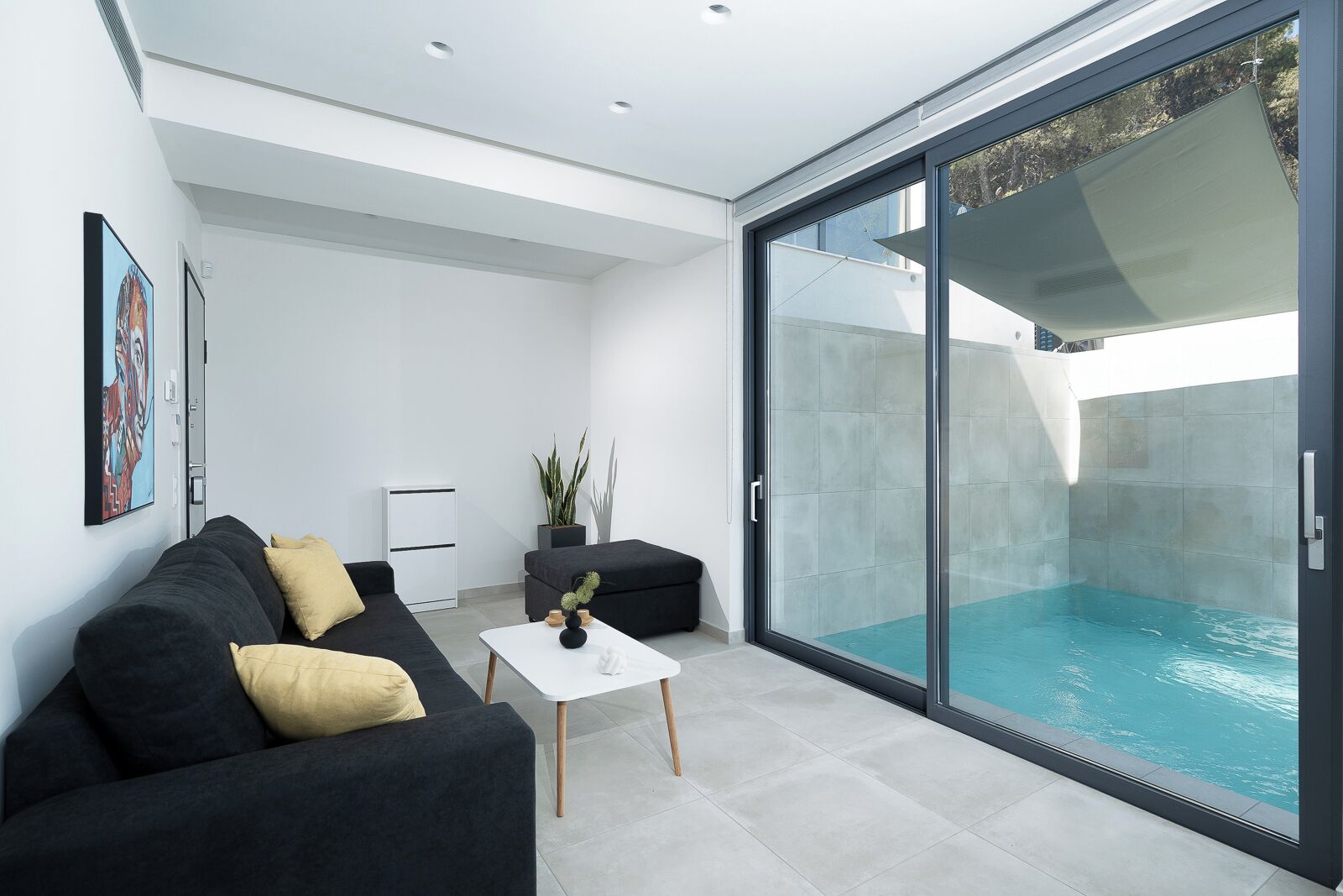 Uma sala de estar moderna com um sofá preto, uma mesa de centro branca e uma porta de vidro que dá para uma piscina.