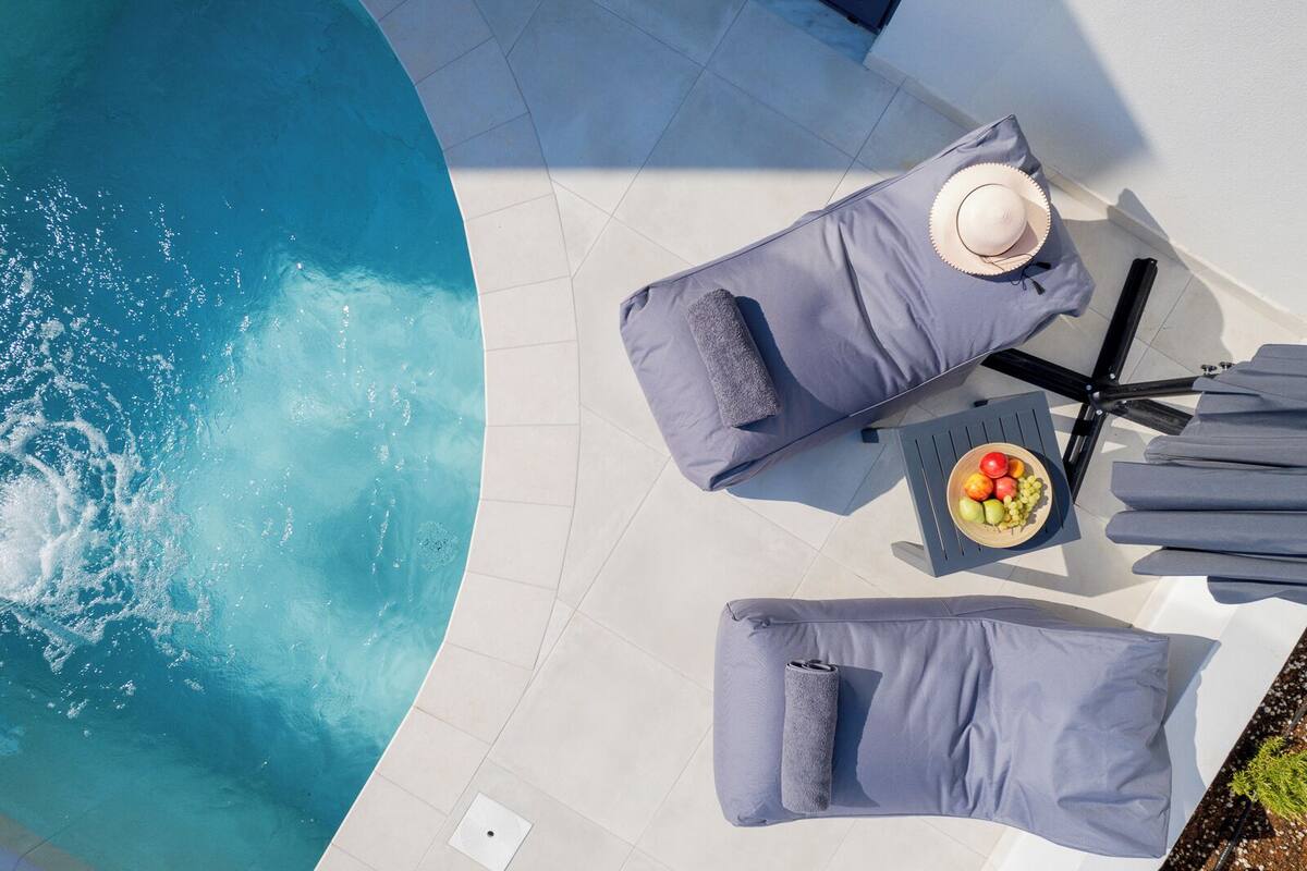 A poolside area with two lounge chairs, a table with a bowl of fruit, and a hat on one of the chairs.