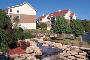 Stroll through a serene garden with a small waterfall and beautifully manicured hedges.