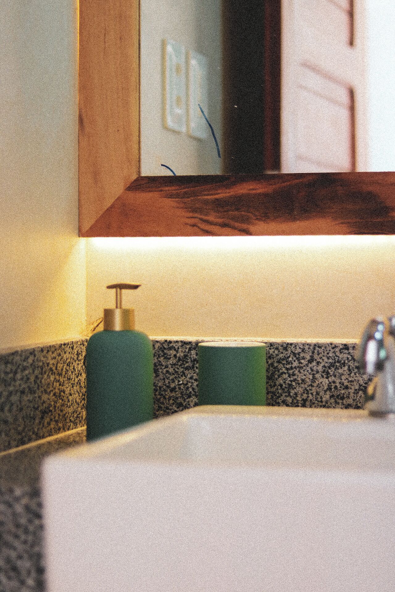 A bathroom with a sink, a mirror, and a green bottle of soap.