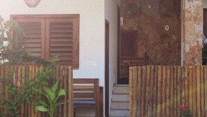 A house with a stone facade, a wooden door, and a small garden area with a bench and plants. - Pousada Casa de Hóspedes (Amontada)