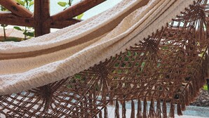 A hammock with a wooden frame and a netted bottom, positioned over a pool with a yellow fence in the background. - Pousada Casa de Hóspedes (Amontada)