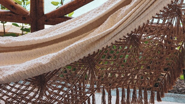 Una hamaca con estructura de madera y base de mosquitero, ubicada sobre una piscina con una cerca amarilla al fondo.