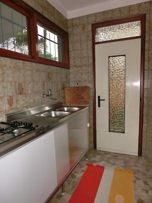 A kitchen with a gas stove, two sinks, a window, and a door with a decorative glass panel.