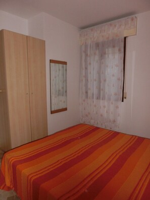 A bedroom with a bed, a wardrobe, a window with curtains, and a mirror on the wall.