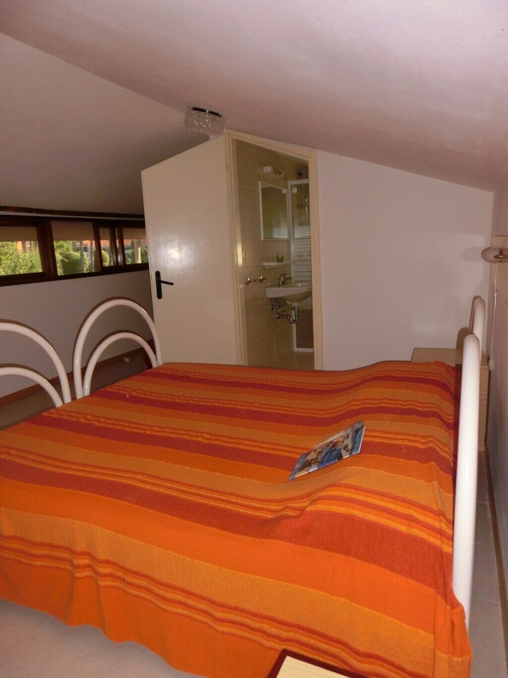 Een kamer met een bed, een raam, een deur en een zichtbare badkamer door de deur.