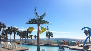 Un área junto a la piscina con sillones de descanso, una palmera y vista al océano.