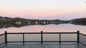 En träveranda med ett räcke som vetter ut mot en stilla sjö i skymningen.