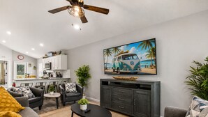 Een woonkamer met een bank, fauteuil, salontafel en een televisie waarop een strandscène te zien is.