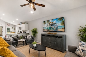 A living room with a sofa, armchair, coffee table, and a TV displaying a beach scene. - 2 Homes Side by Side, Families and Groups Welcome!  Sleeps up to 16 & Courtyard. (St. Augustine)