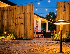 Une clôture en bois, des sièges d’extérieur, des guirlandes lumineuses et un chemin.