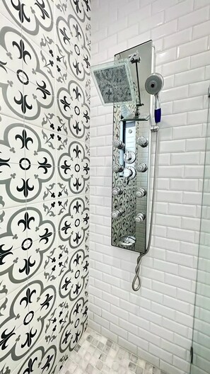 A bathroom with a shower area, a mirror, and a patterned wall.