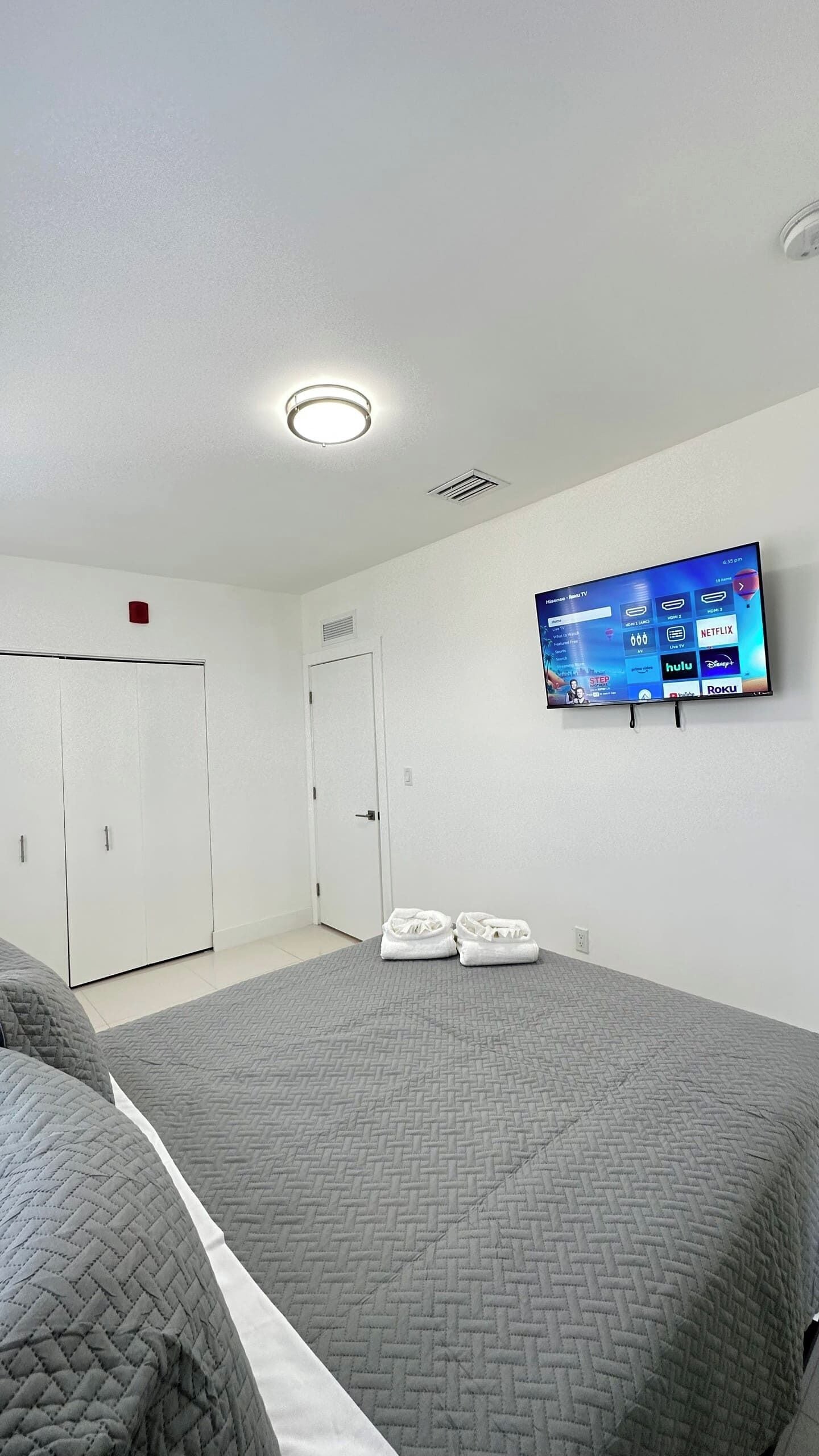 A hotel room with a bed, a television mounted on the wall, a door, and a closet.