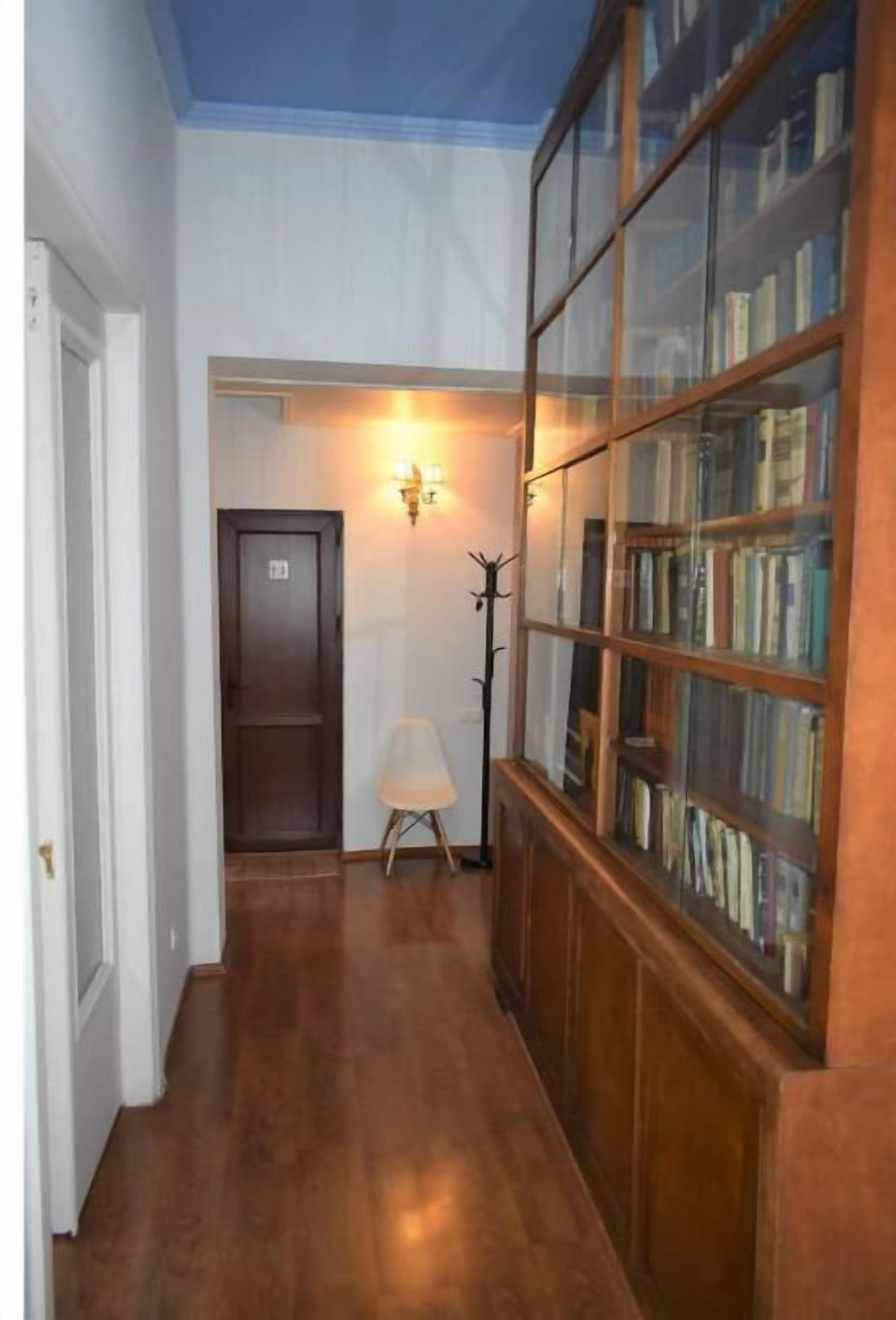 Un couloir doté d’un plancher en bois, d’une bibliothèque en verre et d’un porte-manteau.