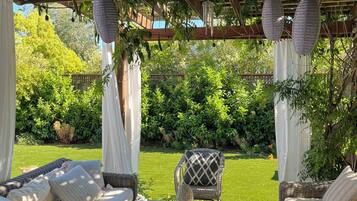 Relax in a serene garden setting with a pergola overhead, wicker sofas, and a round table for a peaceful evening.