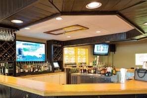 A bar area with a counter, shelves of bottles, and a television screen.