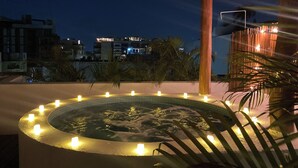 Ein runder Whirlpool mit Beleuchtung am Rand, umgeben von einem Pool und Palmen, unter einer Holzpergola bei Nacht.