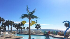 A poolside area with lounge chairs, a palm tree, and a view of the ocean. - Welcome to Paradise! ~ STEPS to BEACH! ~ Sleeps 10 (Panama City Beach)