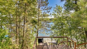 A wooden deck with a table and chairs overlooking a lake, surrounded by trees. - Lakefront Minnesota Escape w/ Fire Pit & Boat Dock (Emily)