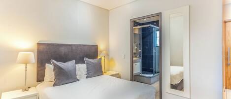 Habitación de hotel con cama, mesitas de noche, un espejo y zona de ducha.