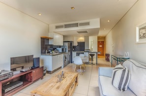 Un salon moderne avec un téléviseur à écran plat, une table basse en bois et un canapé agrémenté d’un coussin à rayures.