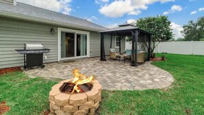 A backyard with a stone fire pit, a grill, and a covered patio area. - Cozy house in a heart of Mandarin (Jacksonville)