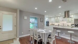 A modern kitchen with a central island, white cabinetry, and a dining area with a round table and chairs. - Cozy house in a heart of Mandarin (Jacksonville)