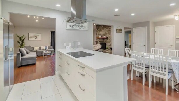 A modern kitchen with a central island, white cabinetry, and a dining area with white chairs. - Cozy house in a heart of Mandarin (Jacksonville)