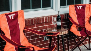 Två utomhusstolar med en vinflaska och ett glas på ett litet bord intill en mur av tegelsten.