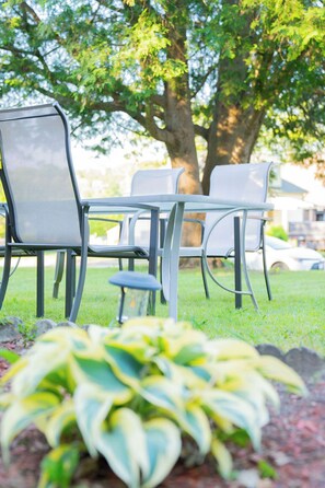 Outdoor seating with metal chairs and a table, surrounded by grass and a tree. - A cozy bunglow in Naigara Falls! (Niagara Falls)