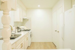 A compact kitchen with white cabinets, a stove, and a sink. - A cozy bunglow in Naigara Falls! (Niagara Falls)