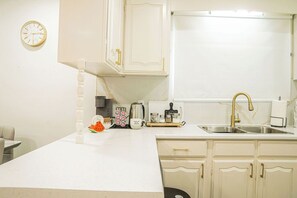 A kitchen with white cabinets, a stainless steel sink, and a clock on the wall. - A cozy bunglow in Naigara Falls! (Niagara Falls)
