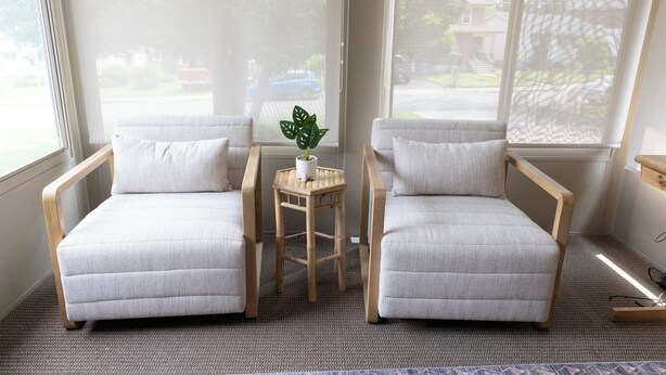A room with two white armchairs, a small wooden table with a potted plant, and large windows with blinds. - A cozy bunglow in Naigara Falls!  (Niagara Falls)