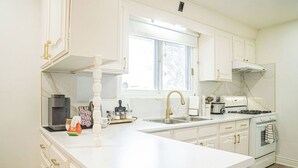 A kitchen with white cabinetry, a large window, and a gas stove. - A cozy bunglow in Naigara Falls!  (Niagara Falls)