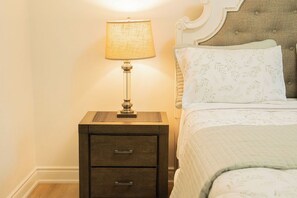A bed with a patterned pillow, a bedside lamp, and a wooden nightstand with drawers. - A cozy bunglow in Naigara Falls!  (Niagara Falls)