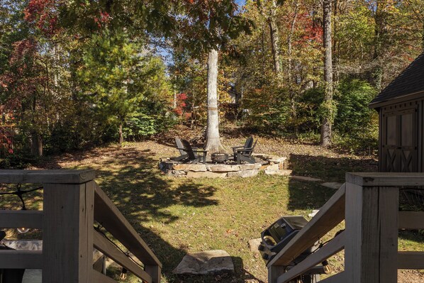 A wooden deck with a stone fire pit and chairs, surrounded by trees with autumn foliage.