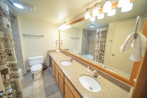Un baño con lavamanos doble, inodoro, ducha y espejo con iluminación.
