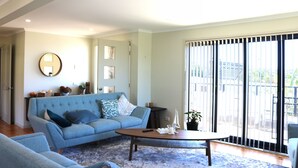 Un salon avec un canapé bleu, une table basse et une grande fenêtre équipée de stores.
