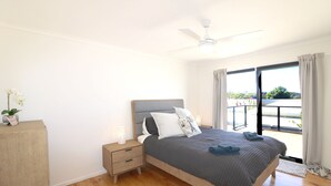 Ein Schlafzimmer mit Bett, Nachttischen, Deckenventilator und Blick ins Freie.