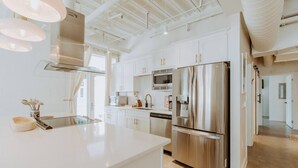 Une cuisine moderne avec des meubles blancs, des appareils en acier inoxydable et des luminaires suspendus.